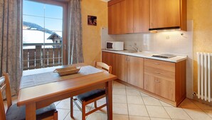 A kitchen with wooden cabinets, a microwave, and a dining table with chairs. - Apartment 'Al Bait Da Marangona 5' with Mountain View, Shared Garden and Wi-Fi (Livigno)