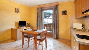 A compact kitchen with a dining area, a television, and a window with curtains. - Apartment 'Al Bait Da Marangona 5' with Mountain View, Shared Garden and Wi-Fi (Livigno)