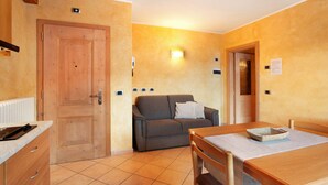A compact room with a wooden door, a sofa, a dining table with chairs, and a tiled floor. - Apartment 'Al Bait Da Marangona 5' with Mountain View, Shared Garden and Wi-Fi (Livigno)