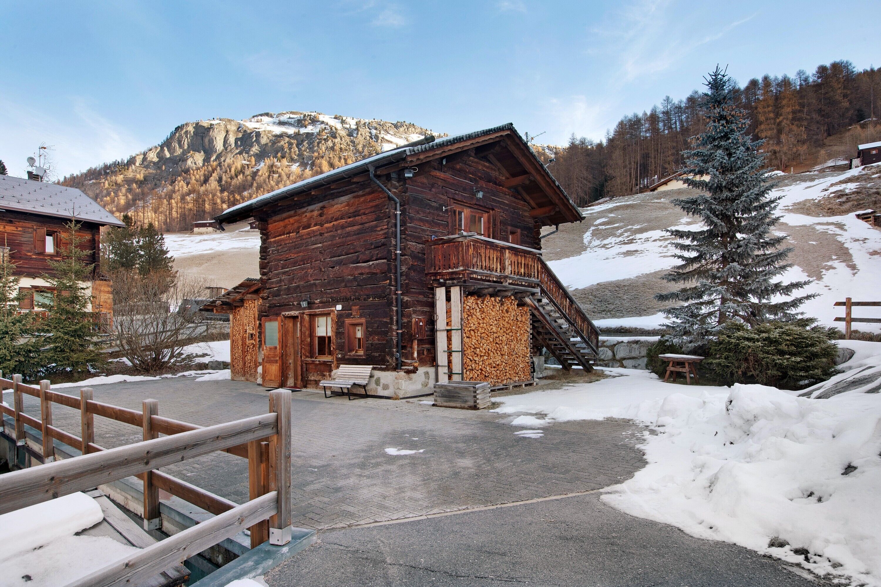 A wooden cabin with a balcony, a staircase, and a view of a snowy mountain.