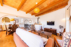 Un vaste espace de vie doté d’un plafond haut, de poutres en bois, d’une table à manger, de chaises, d’un canapé, d’un téléviseur et d’un ventilateur.