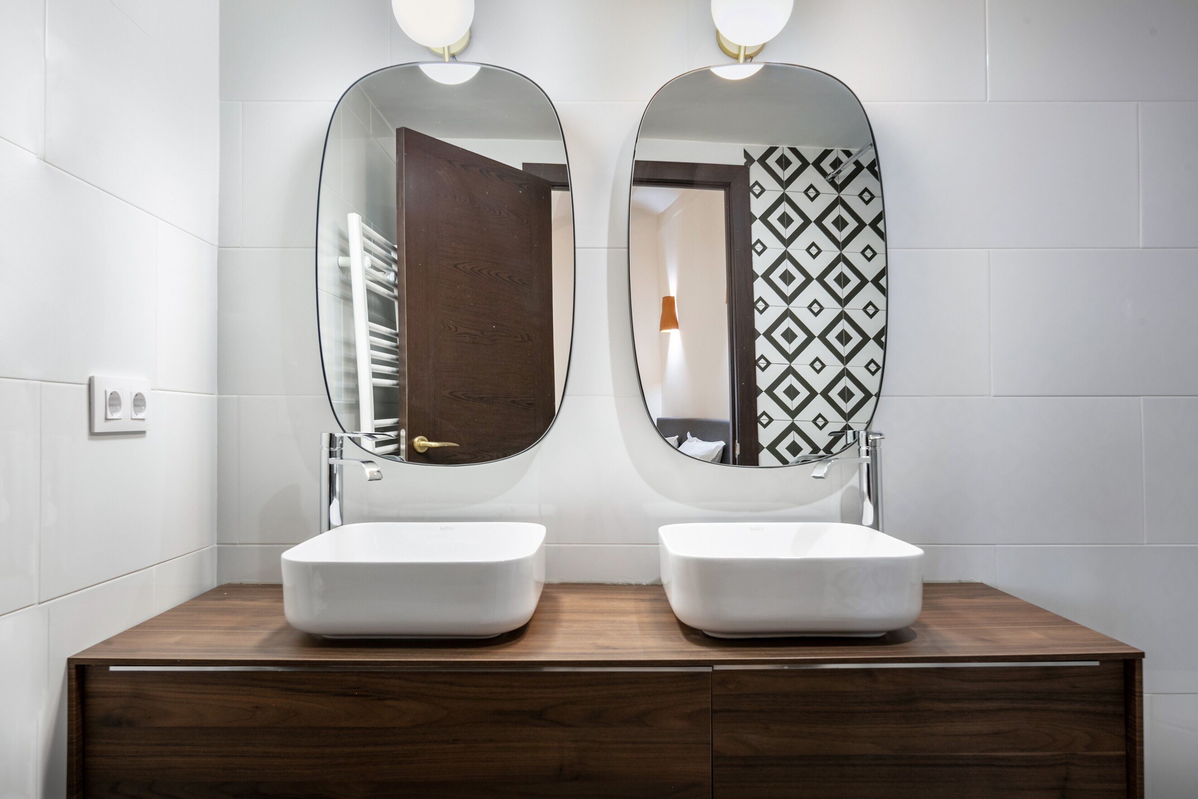 A bathroom with two white sinks, a wooden vanity, and two oval mirrors.