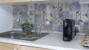 A kitchen with a tiled backsplash, a coffee maker, and a colorful mug on the counter. - Apartment 'Brezza Marina In Oasi Del Mare' with Sea View and Wi-Fi (Granelli)
