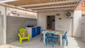 A covered outdoor patio with a table and chairs, a bright green chair, and a kitchen area with a sink and countertop. - Apartment 'Brezza Marina In Oasi Del Mare' with Sea View and Wi-Fi (Granelli)