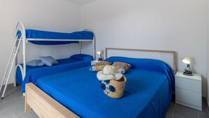 Habitación con literas, cabecera de madera, mesita de noche con lámpara y cesta de mimbre con un sombrero.