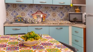 Una cocina con mantel de colores, un bol de tomates verdes y una radio antigua.