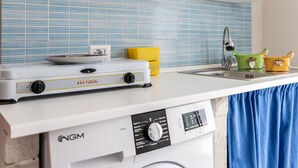 Una cocina con estufa de gas portátil, lavadora y pileta.