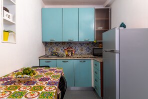 Une cuisine compacte avec des meubles de couleur turquoise, un dosseret à motifs et un petit réfrigérateur.