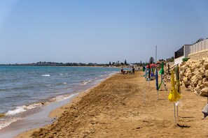 Een zandstrand met een heldere lucht, een rotswand en enkele parasols.