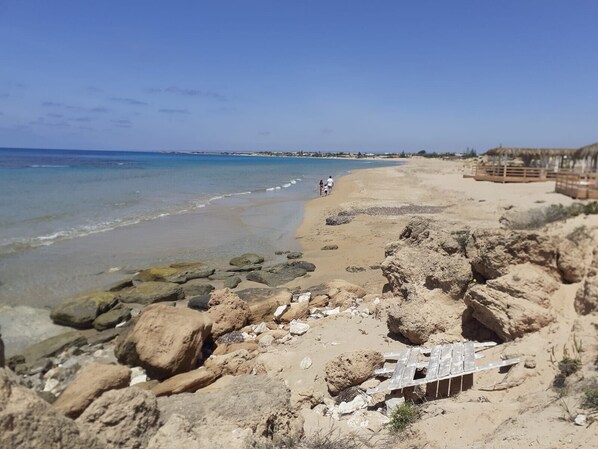 Una playa con terreno rocoso, una estructura de madera y una vista despejada del océano.