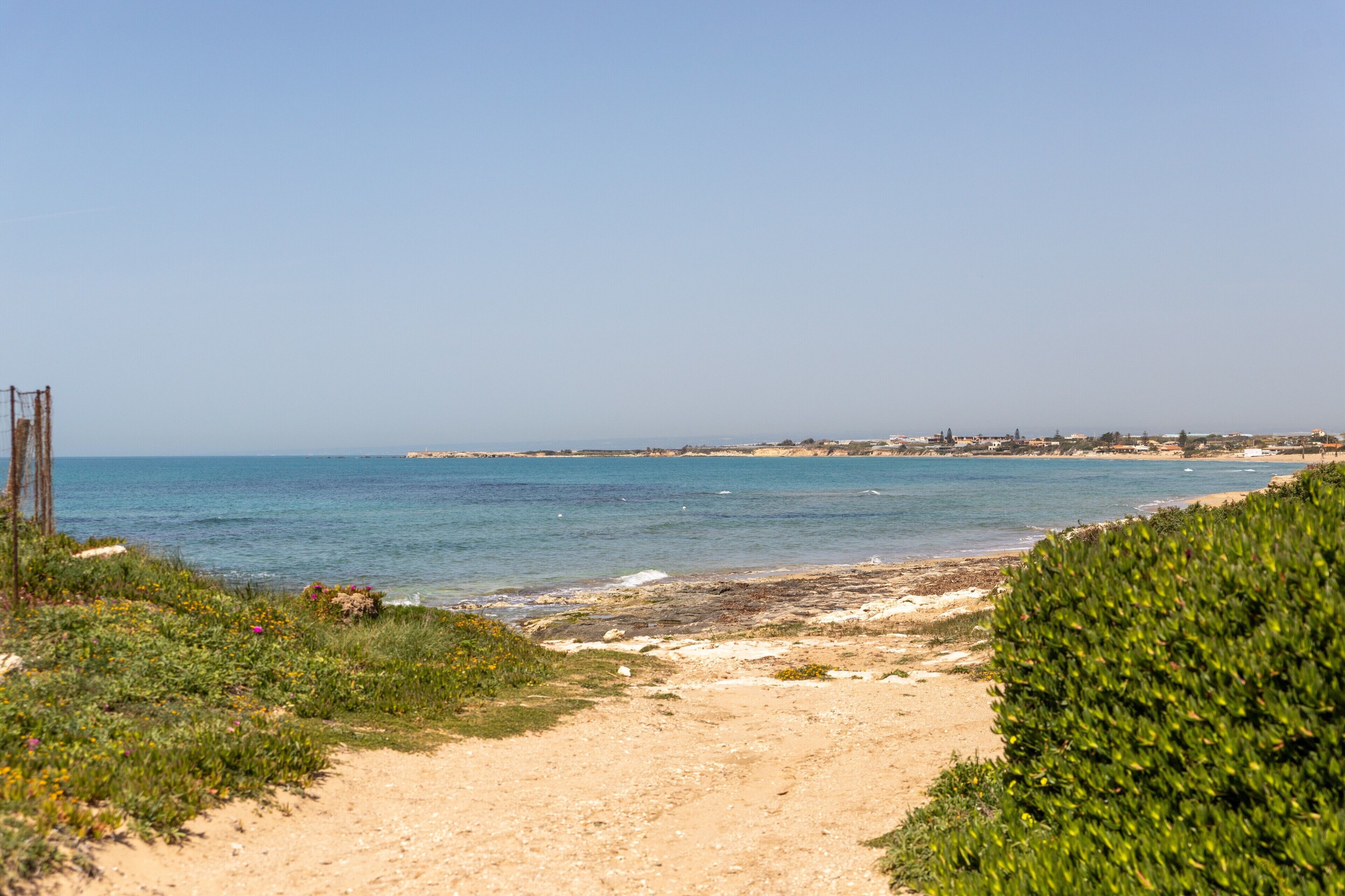 Un sentier côtier menant à une plage, avec un ciel dégagé.