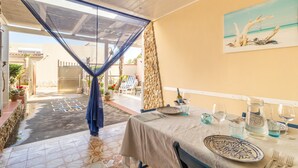 A dining area with a table set for two, a painting on the wall, and a view of the outdoor space. - Holiday Home 'Loft Le Palme' with Private Terrace, Wi-Fi and Air Conditioning (Portopalo di Capo Passero)