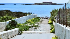 A pathway leading to a coastal area with a view of the sea and a distant structure. - Holiday Home 'Loft Le Palme' with Private Terrace, Wi-Fi and Air Conditioning (Portopalo di Capo Passero)