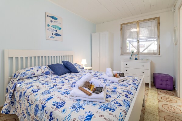 A bedroom with a bed, a dresser, a window, and a wall with a fish painting. - Holiday Home 'Loft Le Palme' with Private Terrace, Wi-Fi and Air Conditioning (Portopalo di Capo Passero)