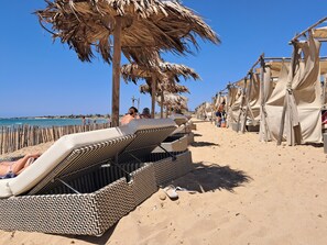 Una playa con tumbonas, sombrillas y cabañas.