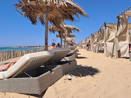 A beach with sun loungers, umbrellas, and beach huts.