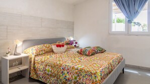 Une chambre à coucher comprenant un lit, une table de chevet, une lampe, une fenêtre avec des rideaux et un mur avec un interrupteur.