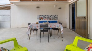 Un espace extérieur abrité, aménagé pour les repas, avec une table, des chaises et un mur recouvert de carreaux.
