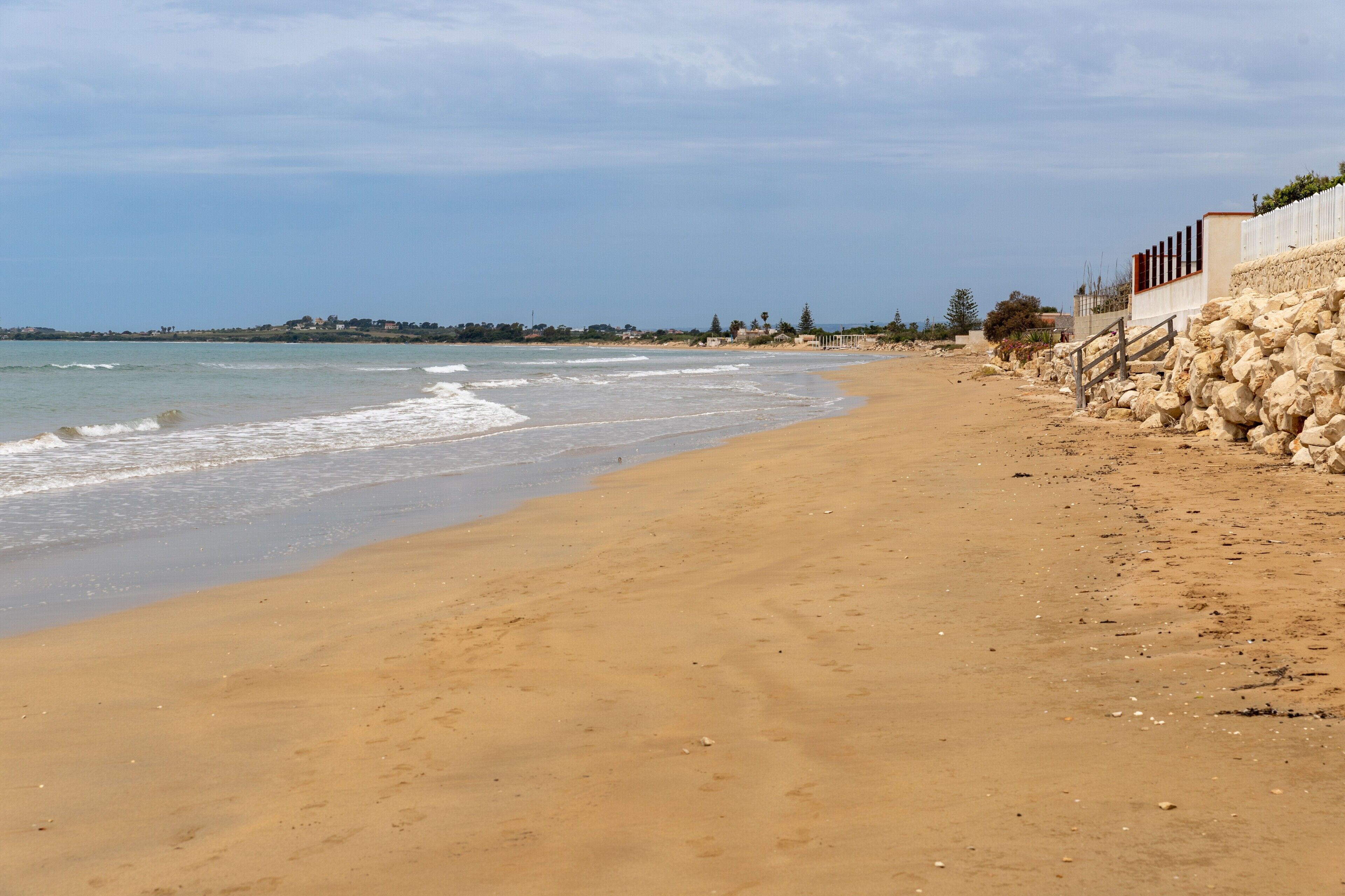 A beach with a sandy shore, a stone wall, and a fence.