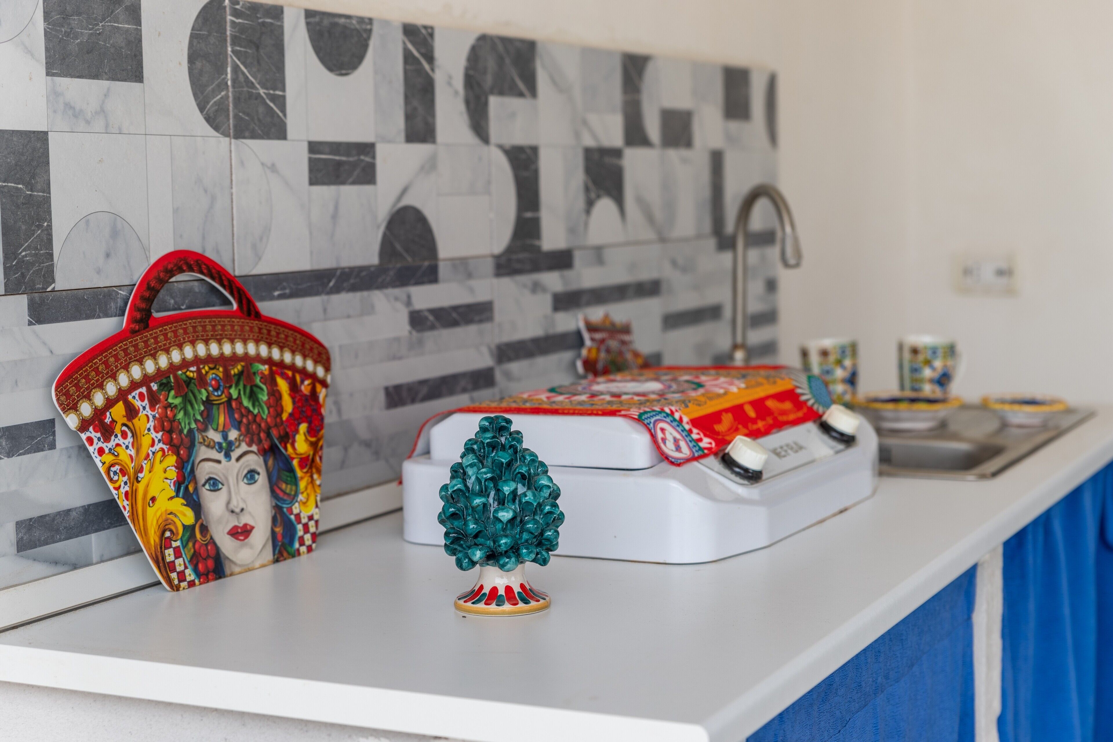Un piano di lavoro in cucina con un oggetto decorativo a forma di albero, un cesto colorato e un elettrodomestico bianco.