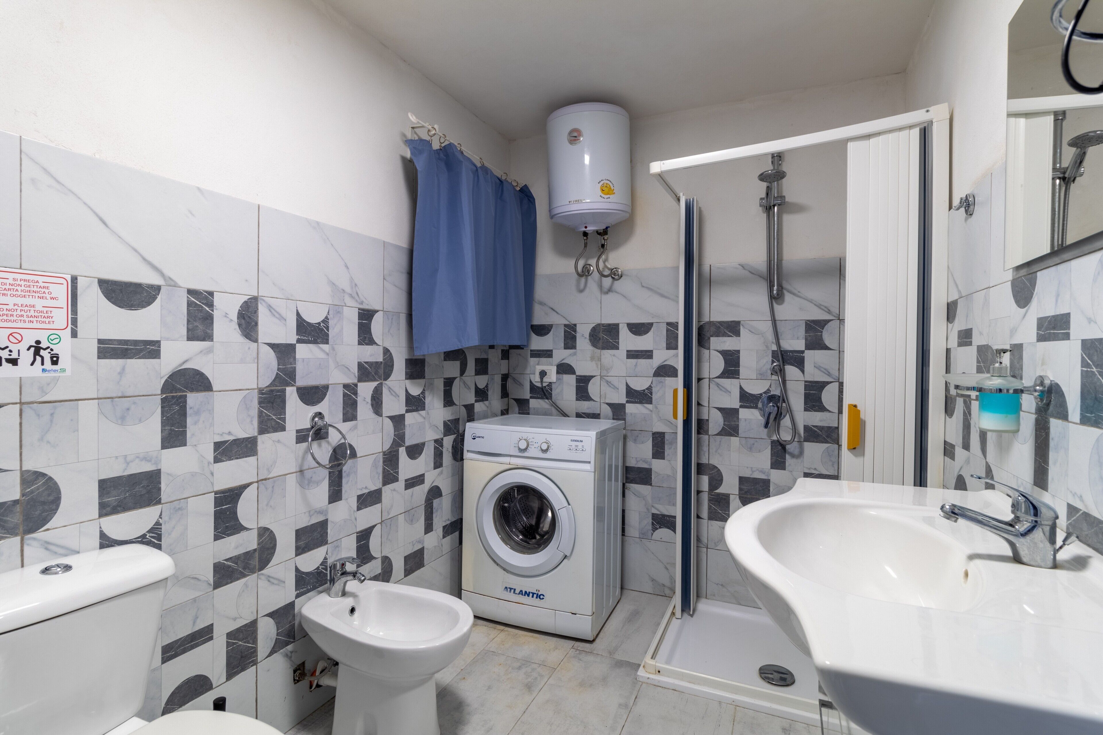 Een kleine badkamer met een wasmachine, bidet en douche.