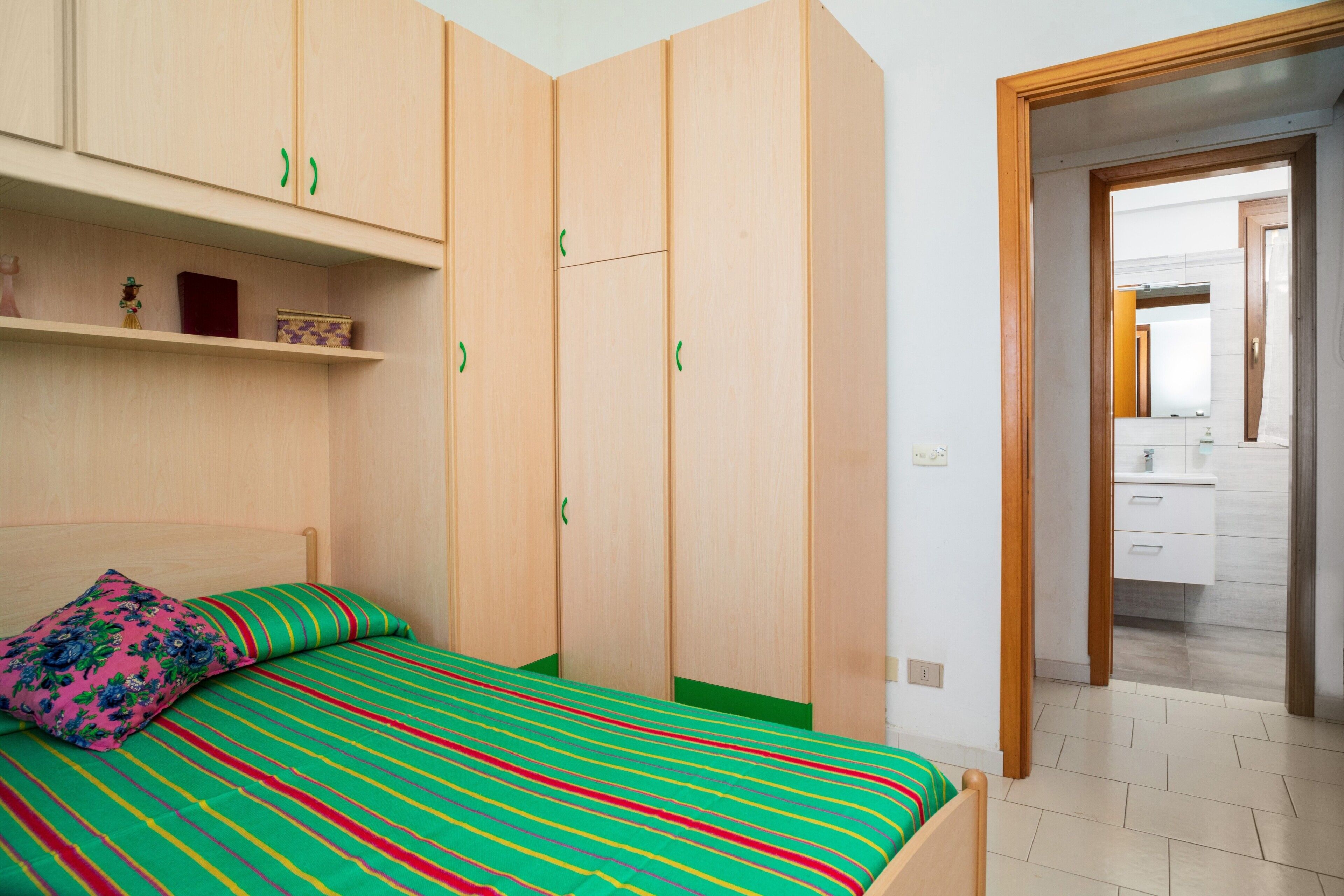 A bedroom with a bed, wooden wardrobe, and a bathroom visible through an open door.