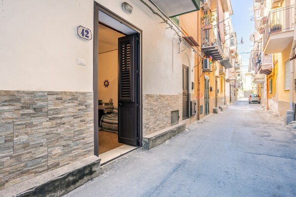 A narrow street with a building entrance, stone wall, and balconies.