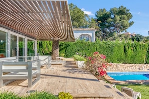 Une terrasse en bois avec des sièges extérieurs, une piscine et un bâtiment doté de grandes fenêtres.