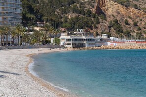 A coastal hotel with a beach view, a pool, and a mountain backdrop.