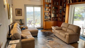 Una sala de estar con sofá, mesa de centro, estantería y vistas a través de un ventanal.
