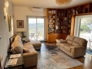 Un soggiorno con divano, tavolino, libreria e vista panoramica attraverso una porta in vetro.