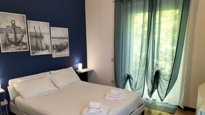 Una cama bien hecha con sábanas blancas, una mesita de noche con una lámpara y tres cuadros en la pared.
