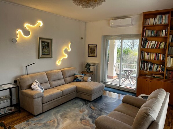 Ein Wohnzimmer mit einer Eckcouch, einem Bücherregal und einem großen Fenster.