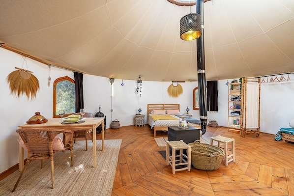 Una habitación acogedora con piso de madera, una cama, una mesa de comedor con sillas, un lámpara colgante y una estantería.