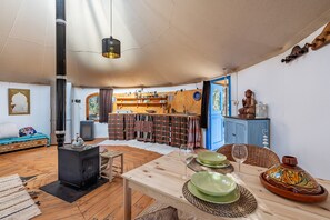 Un salon chaleureux avec un plancher en bois, une table mise avec des assiettes et des verres, un petit poêle et un buffet bleu.
