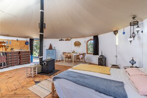 Une pièce confortable avec un lit, une table, une chaise, un poêle et une fenêtre.