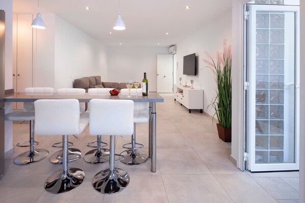 A modern kitchen with a dining area, white furniture, and a TV on the wall.