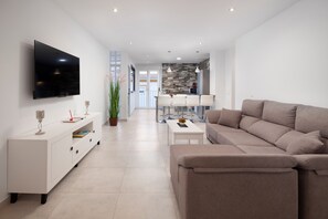 A modern living room with a flat-screen TV, a sofa, a coffee table, and a dining area in the background.
