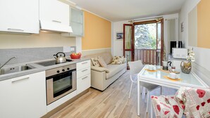 Eine kompakte Küche mit Herd, Spüle und weißen Schränken. Es gibt eine Essecke mit Tisch und Stühlen, sowie ein Sofa.
