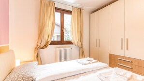 Ein Schlafzimmer mit einem Bett, einem Fenster mit Vorhängen, einem Heizkörper und einem Kleiderschrank.
