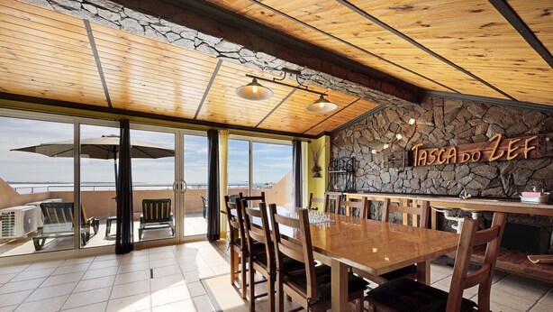 A restaurant with a stone wall, wooden ceiling, and large windows overlooking a scenic view. - Holiday Home 'My Friendly House' with Sea View, Wi-Fi and Air Conditioning (Lagos)