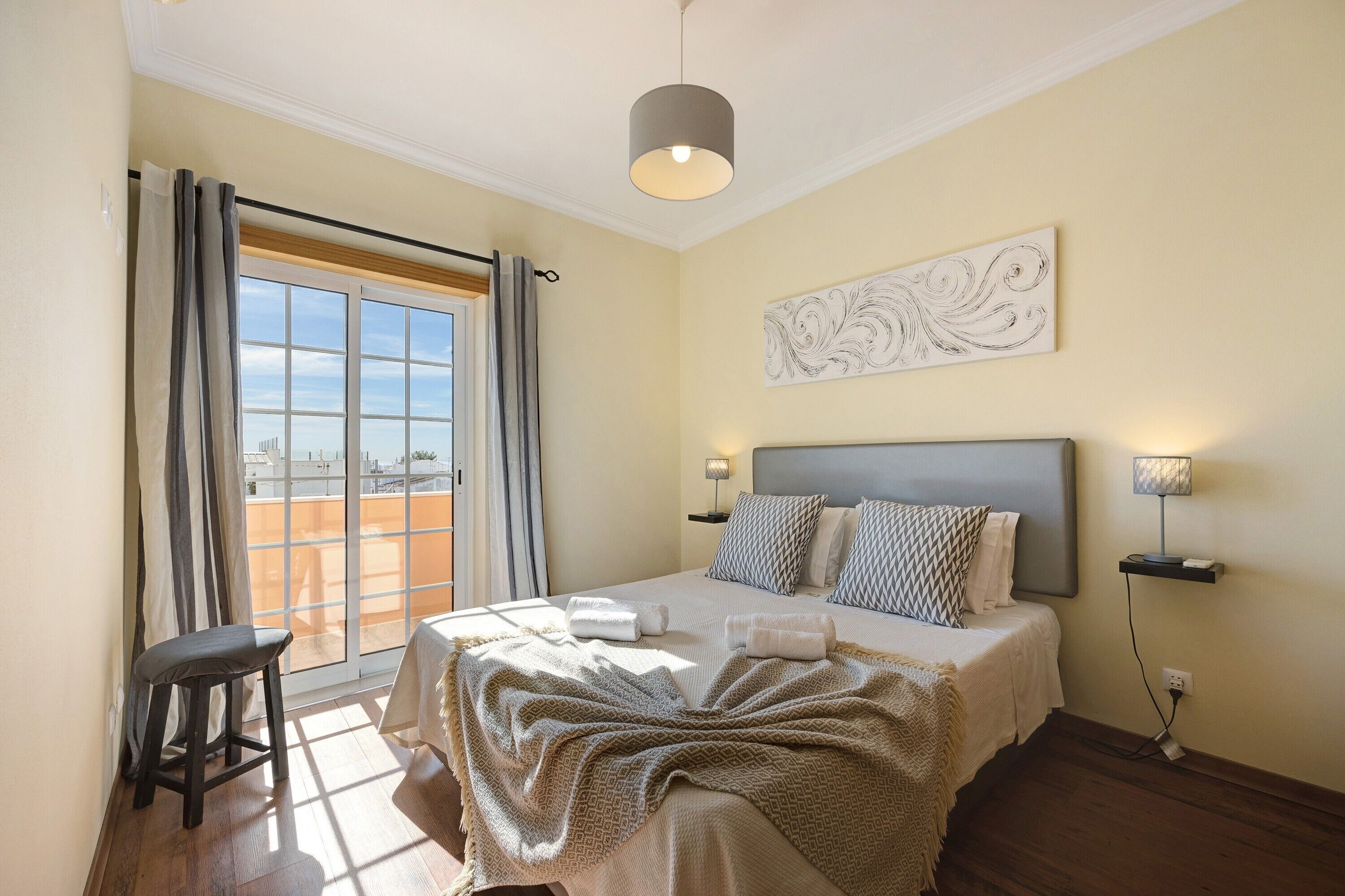 Une chambre à coucher avec un lit, une fenêtre avec des rideaux, une tête de lit, des lampes de chevet et une œuvre d’art accrochée au mur.