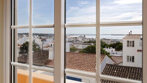 A view through a window with a tiled roof, a white building, and a distant cityscape. - Holiday Home 'My Friendly House' with Sea View, Wi-Fi and Air Conditioning (Lagos)