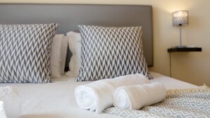 A neatly made bed with patterned pillows, a rolled white towel, and a bedside lamp. - Holiday Home 'My Friendly House' with Sea View, Wi-Fi and Air Conditioning (Lagos)