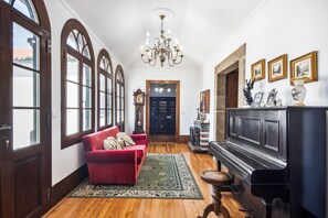 A spacious hallway with a red sofa, a black piano, and a chandelier. - Casa do Terreiro with private pool, private terrace, and Wi-Fi (Barqueiros)