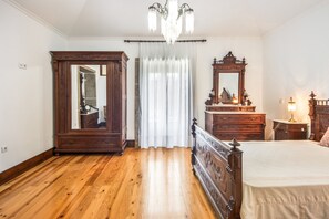 Un dormitorio con piso de madera, una cama grande, un tocador, un espejo y una araña.