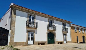 A two-story building with white walls, a red-tiled roof, and black wrought-iron balconies.