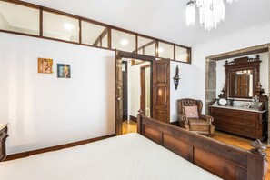 A bedroom with a large bed, a wooden dresser, a chair, and a mirror.