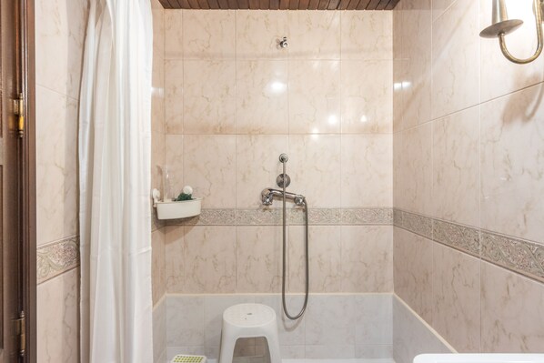 A bathroom with a shower, toilet, and a small shelf with toiletries.