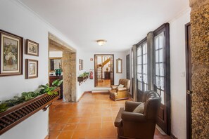 A hallway with a staircase, framed artwork, and a seating area with leather chairs.